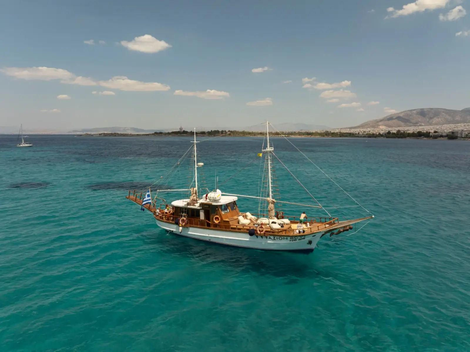 Private wooden cruise boat sailing across the turquoise Athens Riviera coastline
